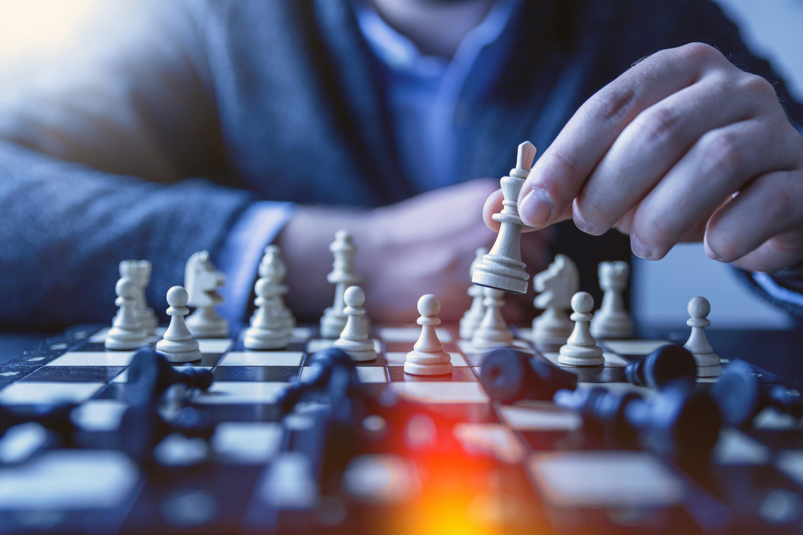 Close-up of a hand making a strategic chess move on a board, emphasizing thought and planning.